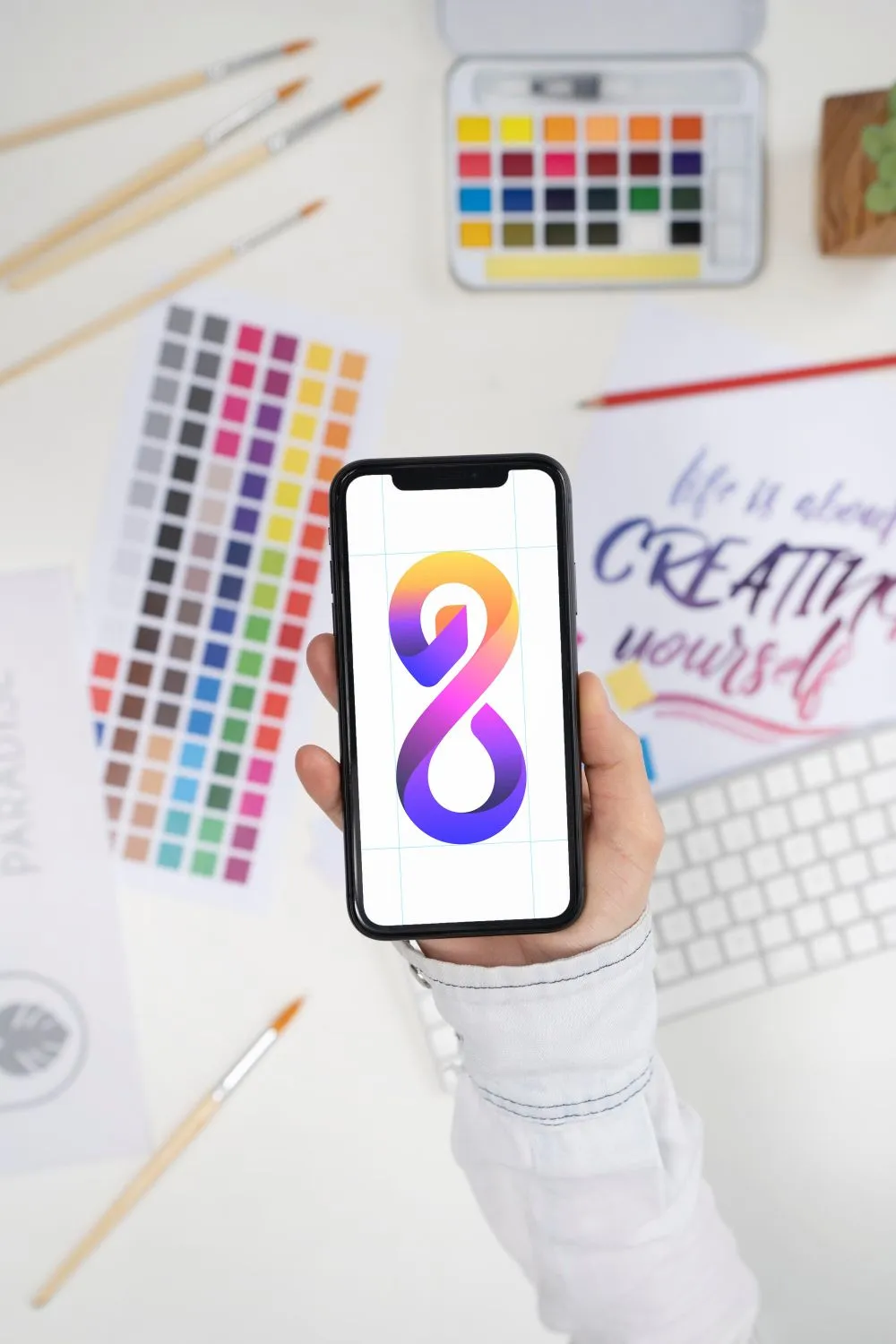Pessoa a segurar smartphone com logótipo no ecrã, rodeado de paletas de cores para desenvolvimento de identidade visual